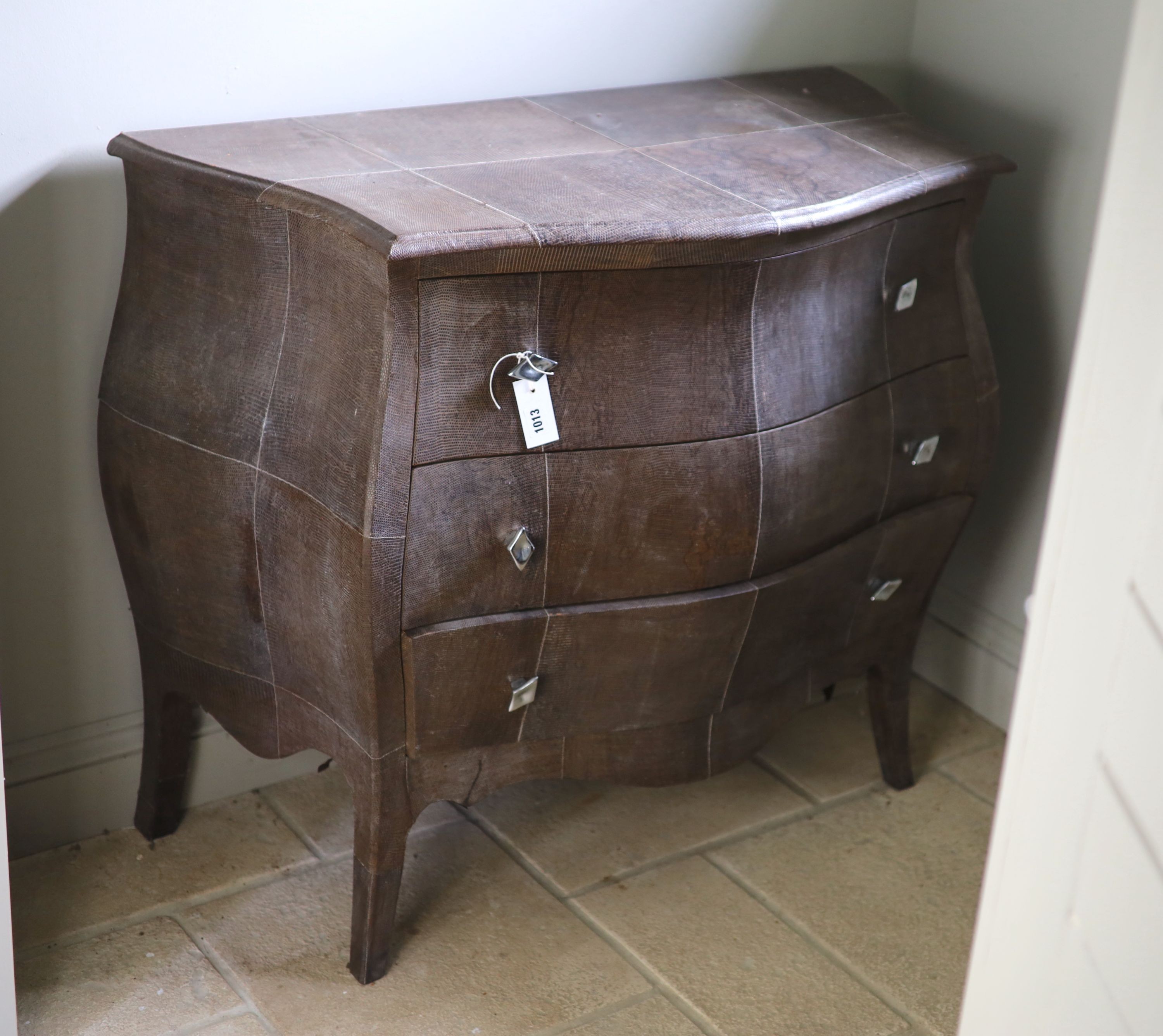 A three drawer bombe commode, upholstered in simulated snake skin, width 102cm depth 51cm height 88cm